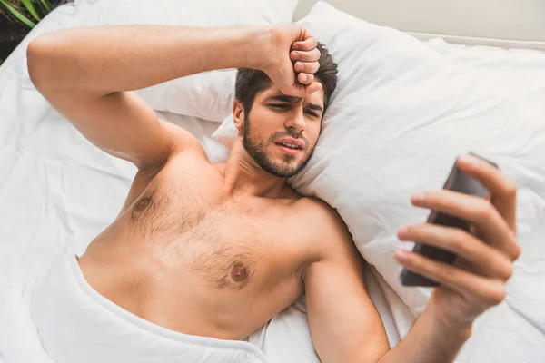 Грустный парень, использующий смартфон в спальне — стоковое фото