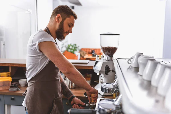 Bebaarde barista aanstampen van gemalen koffie — Stockfoto
