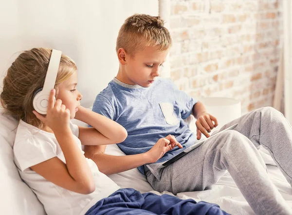 Hermano y hermana sentados con dispositivos electrónicos — Foto de Stock