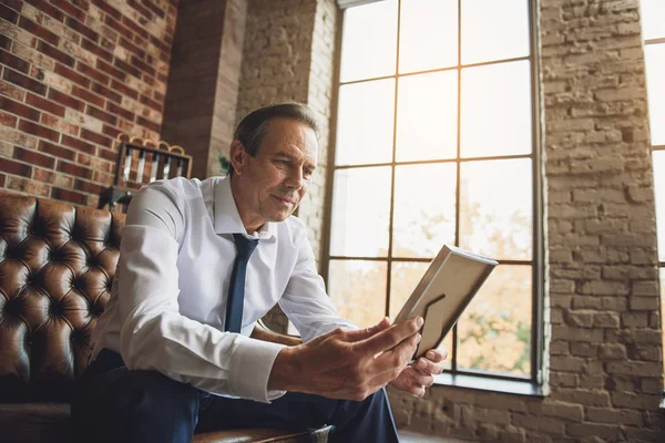 Mature man looking at photo with light sadness — Stock Photo, Image