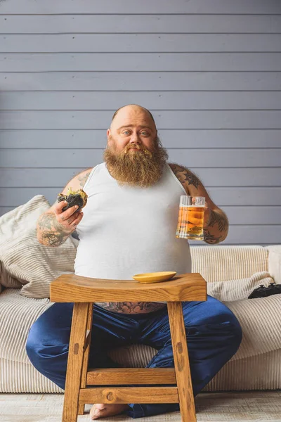 Грустный толстый парень ест сэндвич с алкоголем — стоковое фото