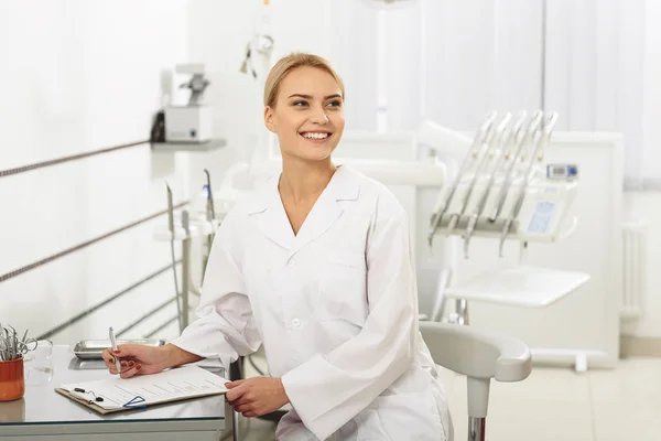 Bonito estomatologista feliz sentado no consultório odontológico — Fotografia de Stock