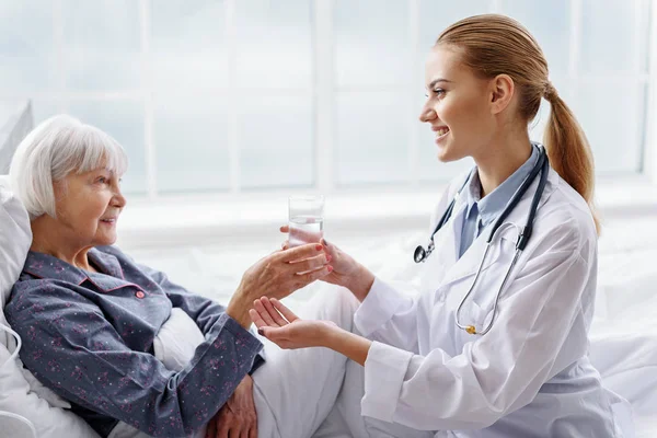 Alegre practicante guardando fuera vaso de agua a la abuela — Foto de Stock