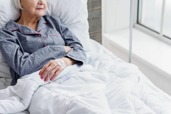 Old woman is on drip flask lying in bed — Stock Photo, Image
