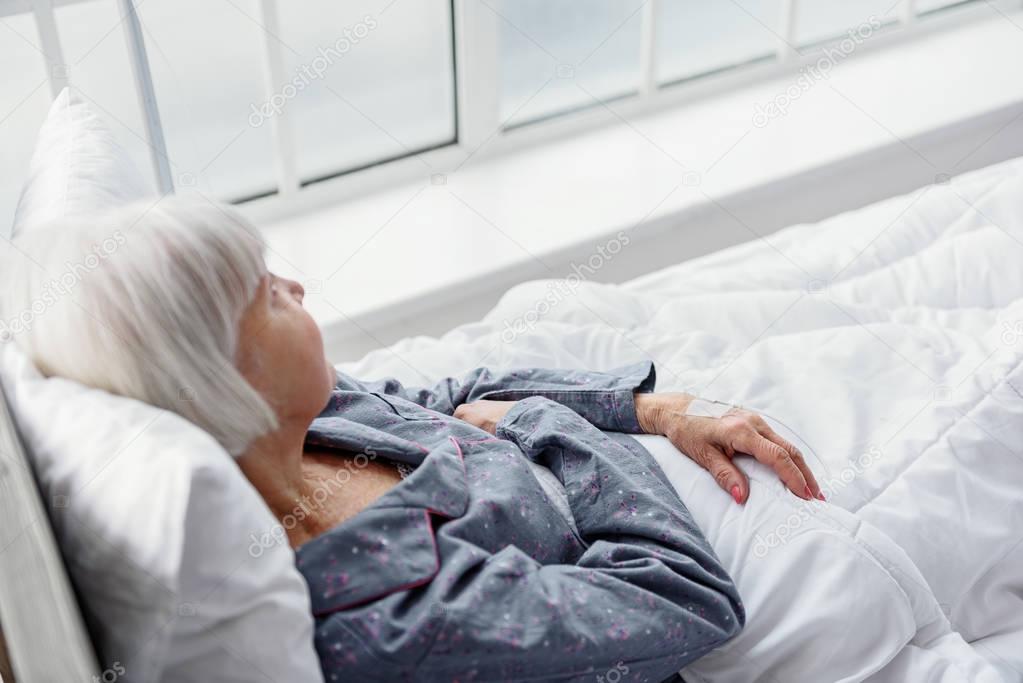 Serene old woman lying on cot in hospital apartment