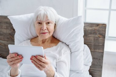 Cheerful granny keeping her tablet in hospital clipart