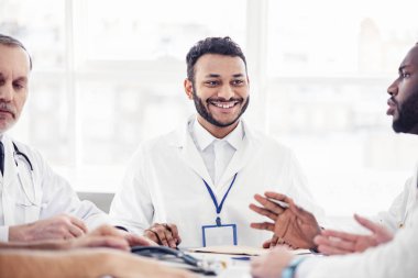 Smiling physician listening his colleagues at meeting clipart