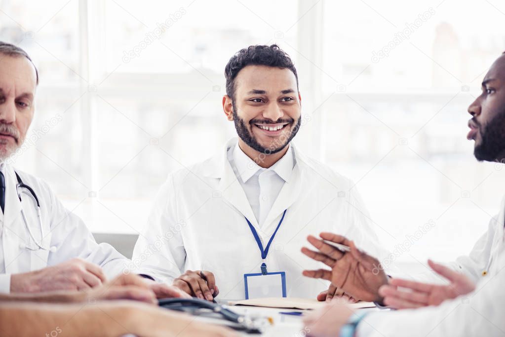 Smiling physician listening his colleagues at meeting