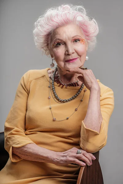 Doamnă în vârstă cu machiaj strălucitor așezat pe scaun Fotografie de stoc