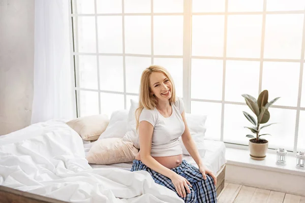 Attractive pregnant woman sitting on edge of bed — Stock Photo, Image