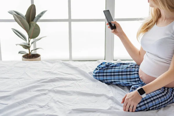 Bela futura mãe usando telefone celular em seu quarto — Fotografia de Stock