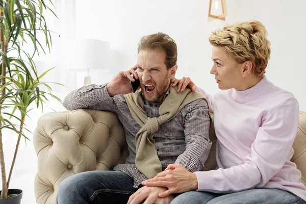 Irritierter Mann spricht mit Smartphone in der Nähe seiner Frau — Stockfoto