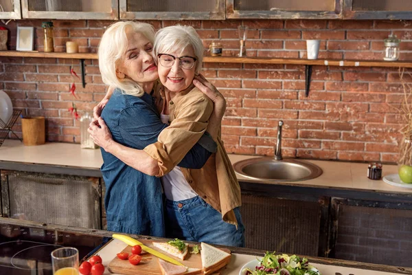 Friendly old ladies embracing during breakfast preparation — Stock Photo, Image