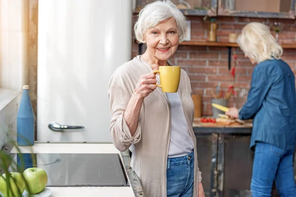 Vrolijke oude dame genieten van warme drank in keuken — Stockfoto