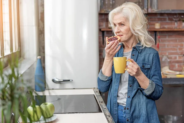 Verträumte Seniorin genießt süßes Essen — Stockfoto