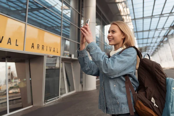 Happy female making pictures by cell phone near airport — стоковое фото