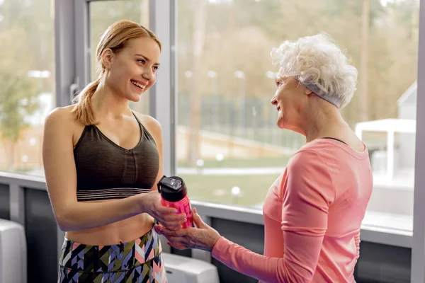 Glückliche Rentnerin nimmt lächelnde Frau mit Mixer-Flasche — Stockfoto