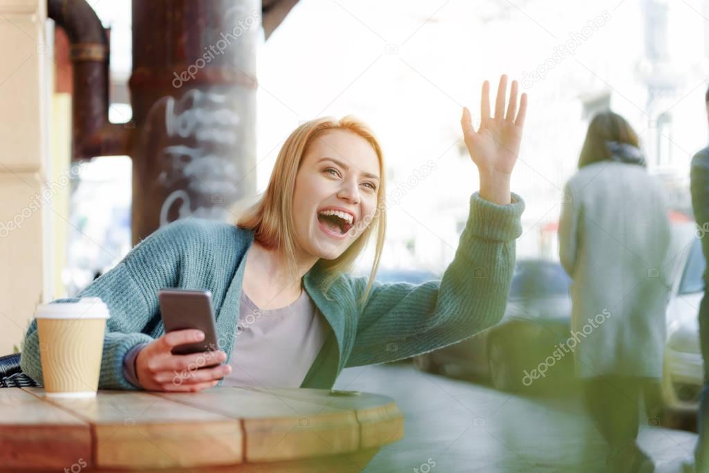 Happy blond girl waving hand to friend on street