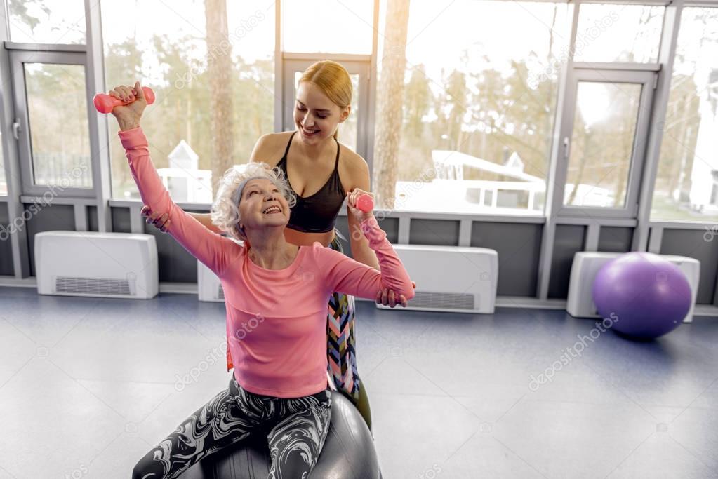 Cheerful retiree making exercises in fitness center