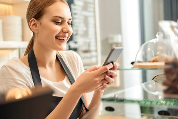 Mensajería de trabajadora feliz en el teléfono inteligente en la cafetería —  Fotos de Stock