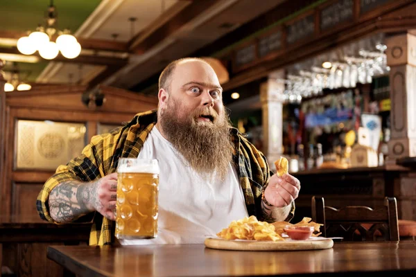 Веселий бородатий чоловік їсть чіпси в барі — стокове фото