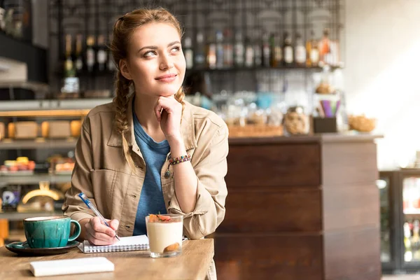 Pensive female writeing in copybook в кафе — стокове фото