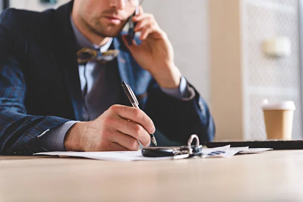 Man schrijven aan tafel tijdens het gesprek op de telefoon — Stockfoto