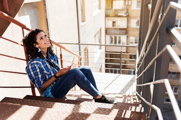 Chica mulata alegre sentado en los escalones con el teléfono celular — Foto de Stock