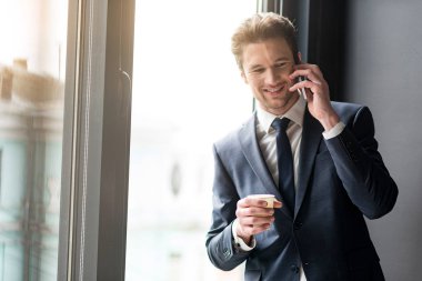 Smartphone üzerinde konuşma yaparken kahve içme neşeli genç adam