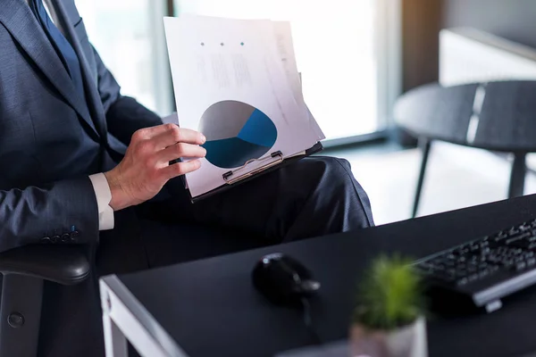 Hombre de negocios adulto en traje está sosteniendo diagramas —  Fotos de Stock