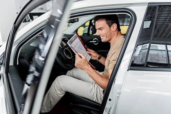 Hombre feliz leyendo información sobre el coche nuevo — Foto de Stock