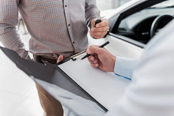 Agent and client filling document in car dealership — Stock Photo, Image
