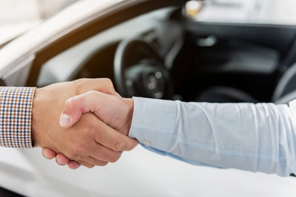 Agent and client clasping arms in car dealership — Stock Photo, Image