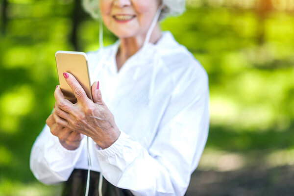 Happy elderly lady using cellphone while exercising outdoors