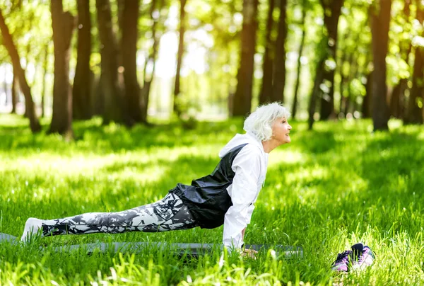 Fröhliche ältere Dame übt auf grünem Gras im Wald — Stockfoto