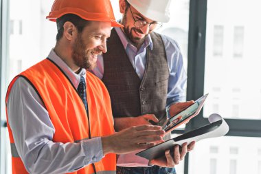 Neşeli gülümseyen inşaatçılar belgelerin incelenmesi