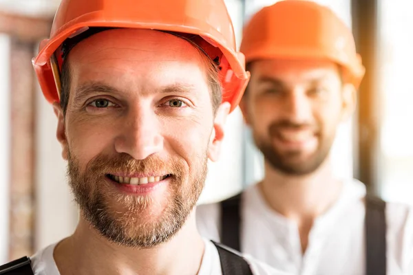Constructores sonrientes alegres en cascos naranjas — Foto de Stock