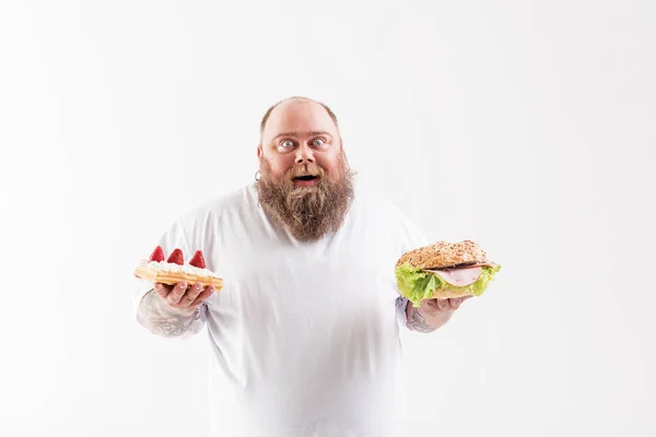 Mutlu kalın adam pasta ve sandviç arasında seçim yapma — Stok fotoğraf