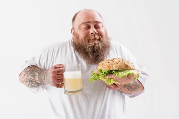 Cheerful thick guy enjoying hold lager with burger — Stock Photo, Image