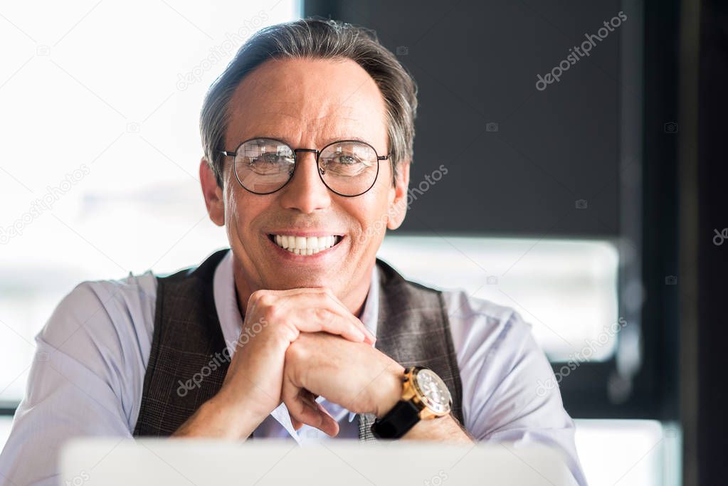 Pleasant mature businessman sitting at table with smile