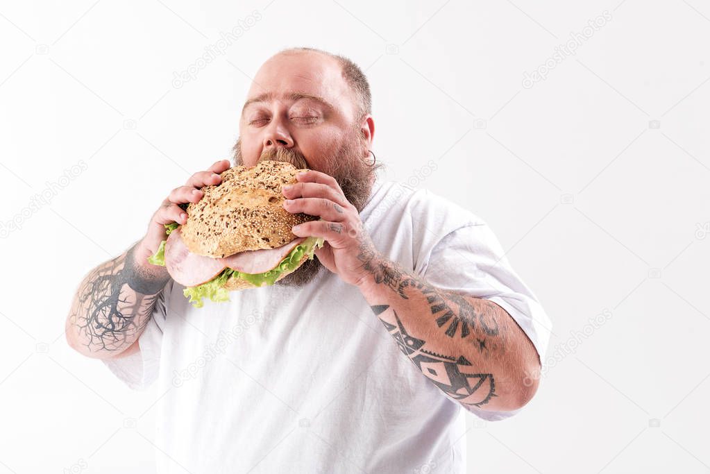 Hungry fat man eating sandwich with appetite