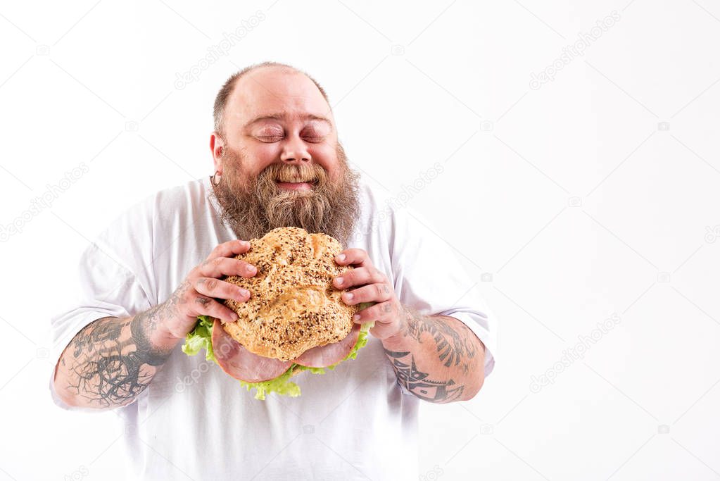 Joyful thick guy eating big bun with meat