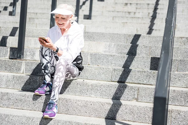 Jolly ανώτερων γυναίκα γραπτών μηνυμάτων μέσω κινητού τηλεφώνου στην πόλη σκάλες με ράγες — Φωτογραφία Αρχείου