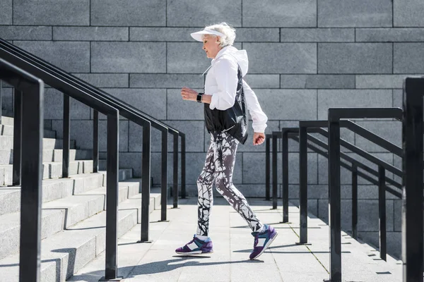 Plechtige senior vrouw joggen buiten op stenen trappen met leuningen — Stockfoto