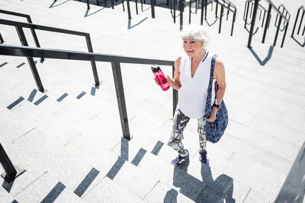 Счастливая старушка забирается наверх после тренировки по каменной лестнице — стоковое фото