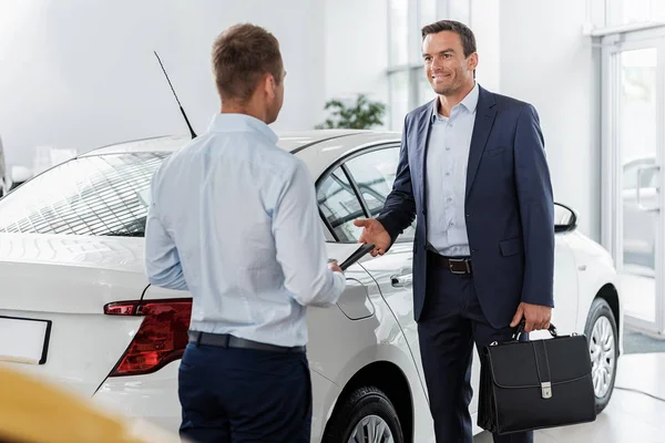 Cheerful male telling with consultant in car dealership — Stock Photo, Image