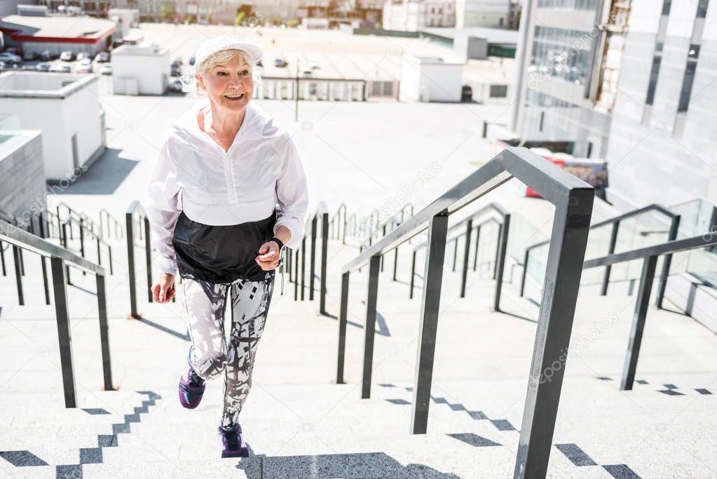 Cheerful aged woman training on steps with guard rails outdoors