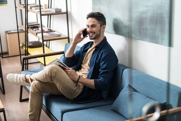 Jolly jeune homme avec barbe relaxant sur le canapé à l'aide d'un téléphone portable — Photo