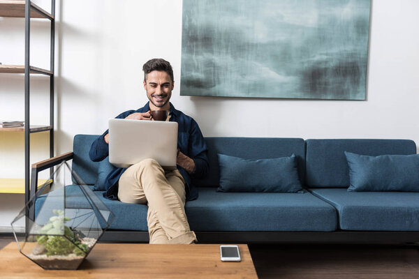 Happy youthful man having rest using notebook at home