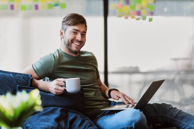 Mutlu genç adam rahat bir atmosferde dizüstü bilgisayar kullanarak